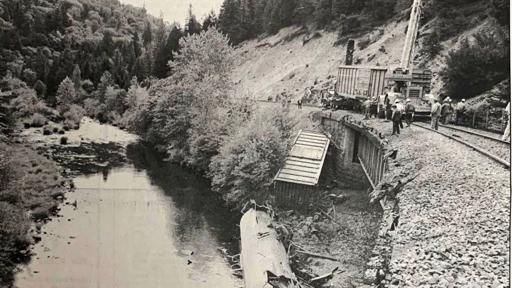 In this photo from the July 17, 1991 edition of the Dunsmuir News, Southern Pacific crews worked to clear tracks of seven cars and an engine that infamously 
derailed days before, spilling thousands of gallons of a weed killer into the Sacramento River. The white tanker that leaked Vapam is shown lying upside down in the water underneath the trestle.