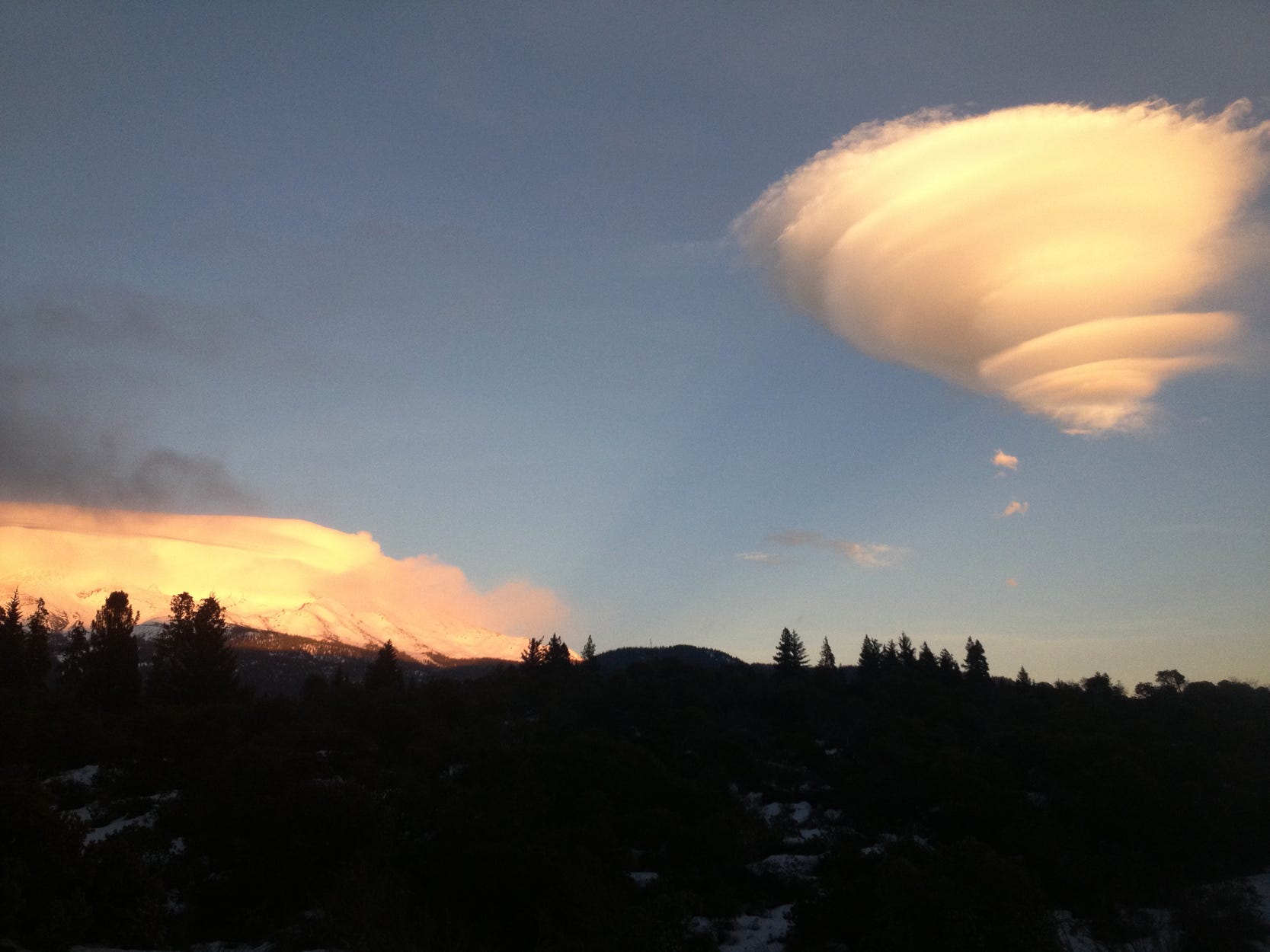 A lenticular approaches Mt. Shasta, which is covered by another lenticular cloud.